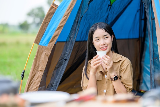 Portret van een gelukkige jonge aziatische vrouw die een water drinkt terwijl ze op een stoel op de camping zit