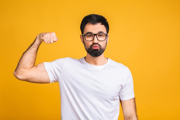 Portret van een gelukkige jonge bebaarde man gekleed in een t-shirt met biceps geïsoleerd op gele achtergrond.