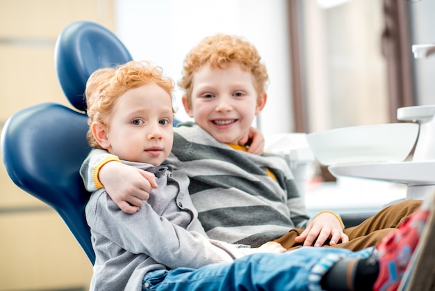 Portret van een gelukkige jonge broers die op de tandartsstoel bij de tandartspraktijk zitten