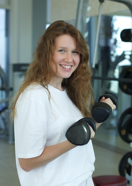 Portret van een gelukkige jonge fitte sportieve vrouw die traint in de sportschool en naar de camera kijkt en in het wit glimlacht