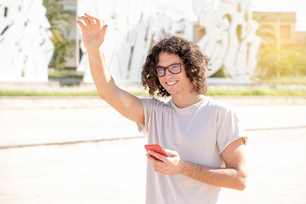 Portret van een gelukkige jonge italiaanse knappe man zegt hallo, houdt een smartphone vast in een wit overhemd