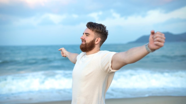 Portret van een gelukkige jonge knappe man met een baard op de zee of oceaan die op het strand loopt en geniet van goed zomerweer op vakantie in tropisch land