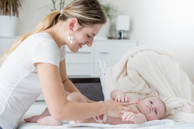 Portret van een gelukkige jonge moeder die de luiers van haar baby op bed verandert