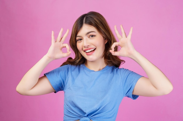 Portret van een gelukkige jonge vrouw die een casual t-shirt draagt met een goede keuze voor een oksign-advertentie, geïsoleerd over een roze achtergrond