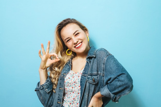 Portret van een gelukkige jonge vrouw die gebaren voorstellen en over muur glimlachen