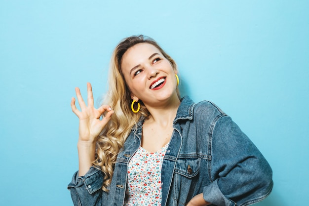 Portret van een gelukkige jonge vrouw die gebaren voorstellen en over muur glimlachen