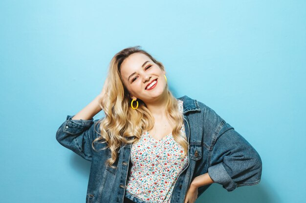 Portret van een gelukkige jonge vrouw die gebaren voorstelt en over blauwe muur glimlacht