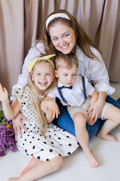 Portret van een gelukkige jonge vrouw die met haar zoon en dochter op de grond zit en ze knuffelt