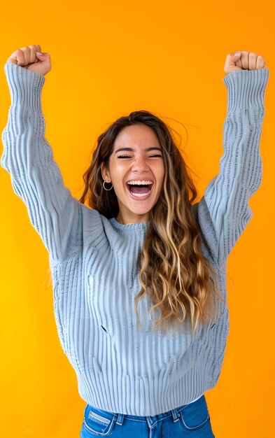 Portret van een gelukkige jonge vrouw die succes viert dat over gele achtergrond wordt geïsoleerd