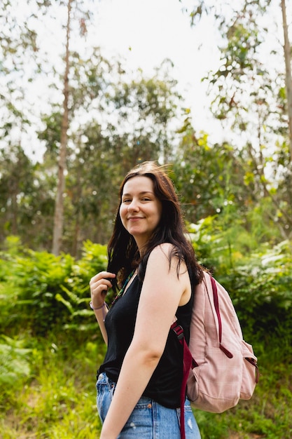 Portret van een gelukkige jonge vrouw in een t-shirt en met zwart haar en een roze rugzak tijdens een wandeling in de natuur