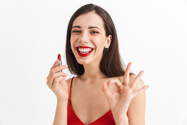 Portret van een gelukkige jonge vrouw in geïsoleerde kleding, die rode lippenstift houdt