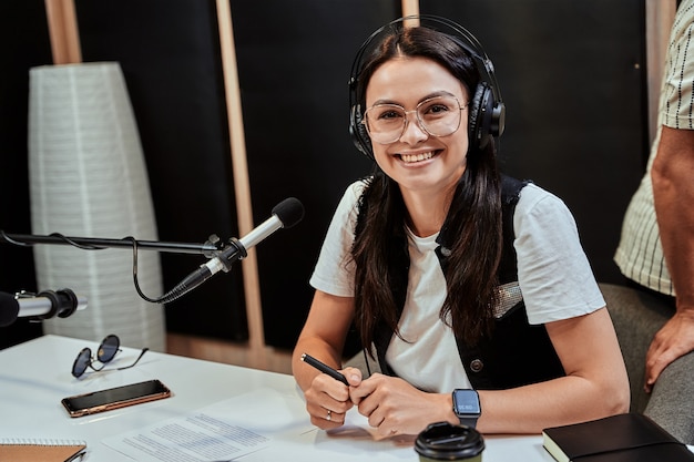 Portret van een gelukkige jonge vrouwelijke radiopresentator die naar de camera glimlacht tijdens het uitzenden in de studio