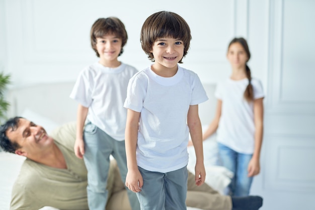 Portret van een gelukkige kleine latijns-jongen die naar de camera glimlacht terwijl hij thuis plezier heeft met zijn vader en broers en zussen. gelukkige jeugd, ouderschapsconcept