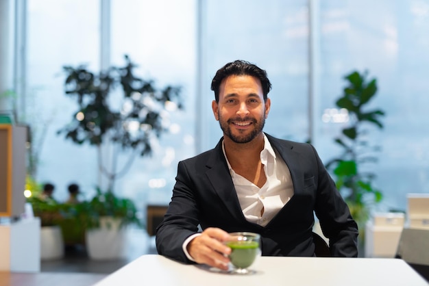 Portret van een gelukkige knappe Spaanse zakenman in de coffeeshop met groene thee