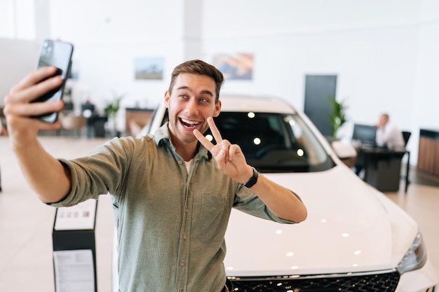 Portret van een gelukkige koper die een selfie maakt met een overwinningsbord op een smartphone van een autodealer