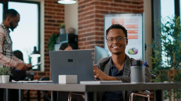 Portret van een gelukkige man die laptop gebruikt om aan bedrijfsstatistieken te werken, bedrijfsgrafieken te analyseren met gegevens voor ontwikkelingsoplossing. jongere met een handicap op kantoorbaan. uit de hand geschoten.