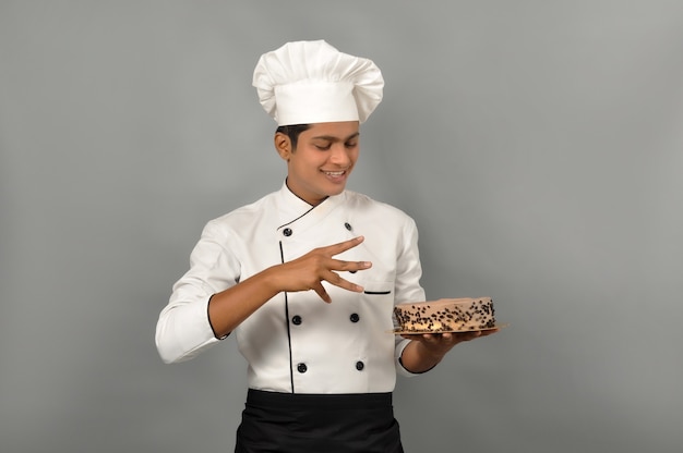 Portret van een gelukkige mannelijke chef-kok gekleed in uniforme holdingsplaat met chocoladetaart met goochelaar pose