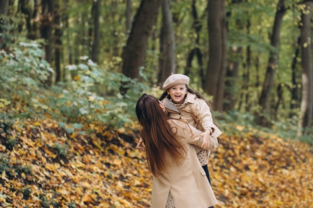 Portret van een gelukkige moeder en dochter die samen tijd doorbrengen in het herfstpark met vallende gele bladeren