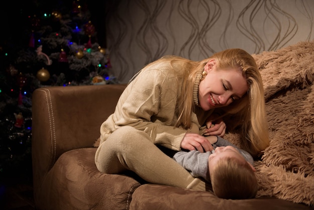 Portret van een gelukkige moeder en een schattige baby die thuis op de achtergrond van een kerstboom speelt.