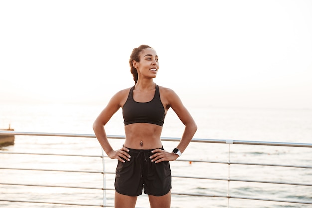 Portret van een gelukkige mooie vrouw in sportieve kleding die opzij kijkt terwijl ze 's ochtends aan zee staat