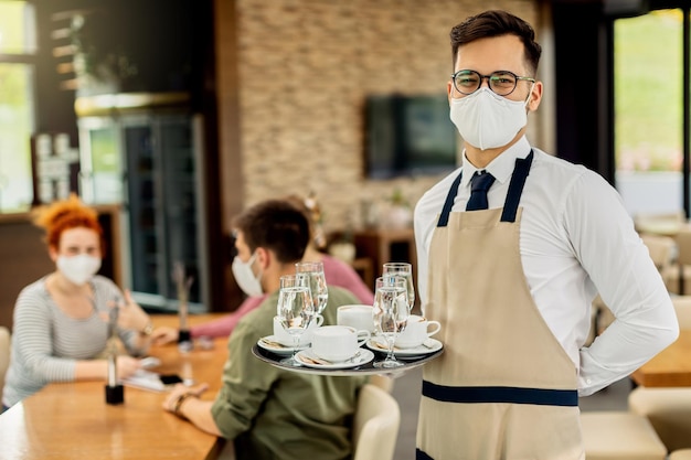 Portret van een gelukkige ober met beschermend gezichtsmasker die koffie serveert in een café