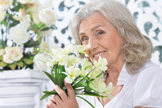 Portret van een gelukkige oudere vrouw die met bloemen poseert