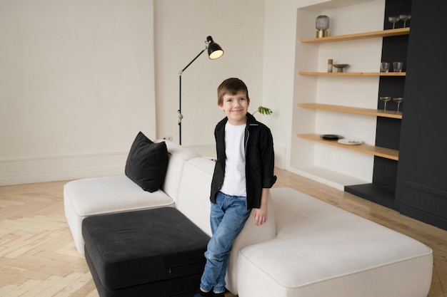 Portret van een gelukkige peuterjongen in een zwart shirt in het interieur van een appartement in de buurt van een witte bank