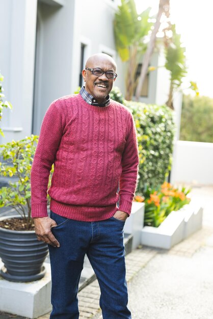 Foto portret van een gelukkige senior afro-amerikaanse man met een bril en een rode trui die buiten het huis staat