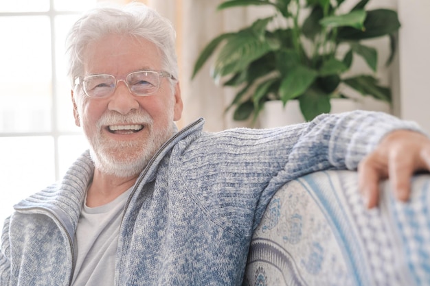 Portret van een gelukkige senior man met een bril die glimlacht en naar de camera kijkt Oude man die thuis op de bank ontspant Portret van een oudere man die geniet van zijn pensioen