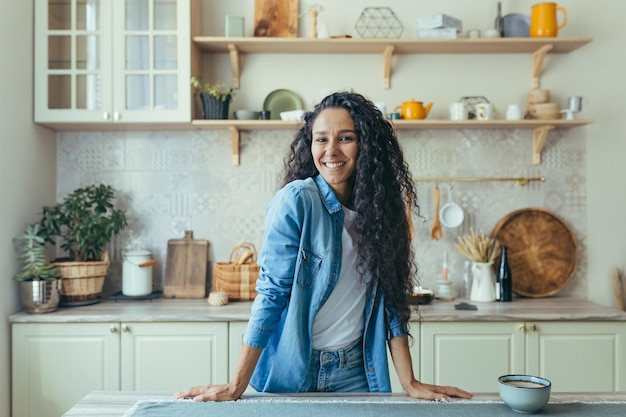 Portret van een gelukkige Spaanse vrouw thuis in de keuken vrouw met krullend haar glimlachend en kijkend