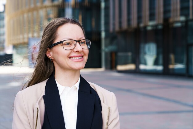 Portret van een gelukkige succesvolle vrouw met een blanke etniciteit in een bril staat in een jas en pak tegen