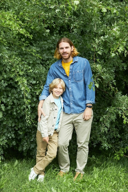 Portret van een gelukkige vader en zoon die tegen het groen in het park staan en naar de camera kijken