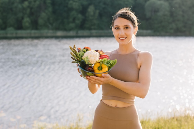 Portret van een gelukkige veganistische vrouw met een bord verse groenten buitenshuis