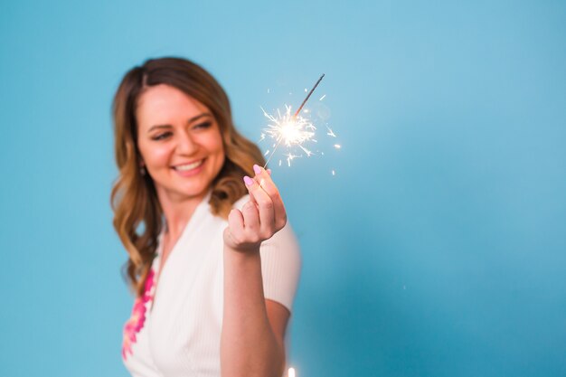 Portret van een gelukkige vrouw die bengaalse lichten over blauwe achtergrond met exemplaarruimte houdt. kerstmis, vieringen en vakantieconcept