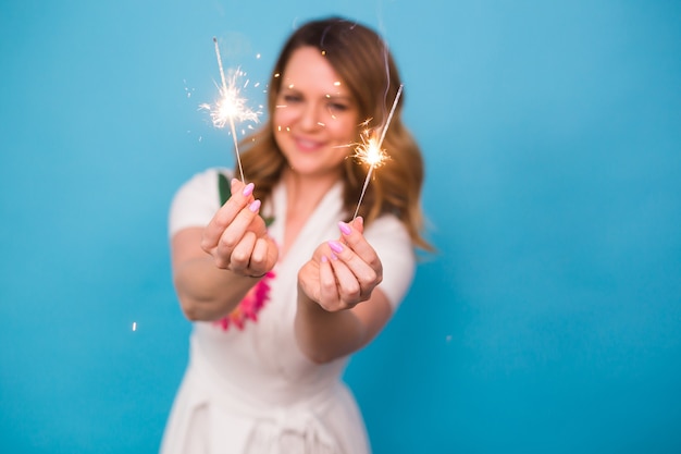 Portret van een gelukkige vrouw die Bengaalse lichten over blauwe achtergrond met exemplaarruimte houdt. Kerstmis, vieringen en vakantieconcept