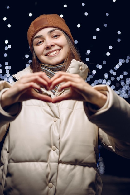 Portret van een gelukkige vrouw die een hartliefde-teken toont en naar de camera kijkt in de winter op straat in de stad