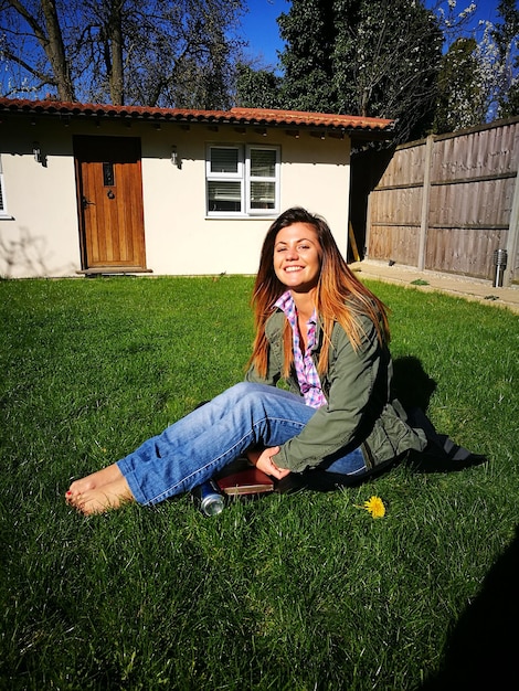 Portret van een gelukkige vrouw die op een zonnige dag op het gras in de tuin zit