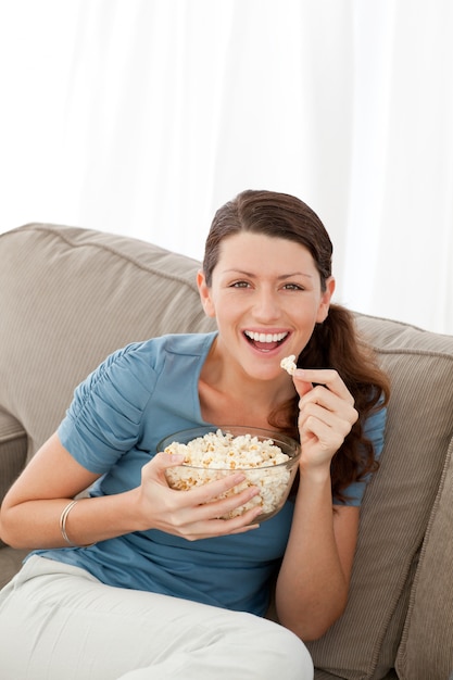Portret van een gelukkige vrouw die popgraan eet terwijl het letten van op televisie
