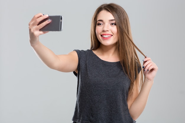 Portret van een gelukkige vrouw die selfie foto maakt op smartphone geïsoleerd op een witte achtergrond