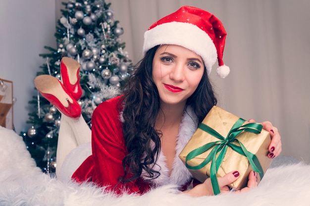 Portret van een gelukkige vrouw in een kerstmandoek die veel geschenkdozen knuffelt op de achtergrond die is ingericht voor het kerstappartement. meisje met kerstcadeau op het bed is blij en ulybaetsya.