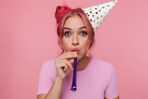 Portret van een gelukkige vrouw met een kleurrijk kapsel met een feestkegel die in een fluitje blaast