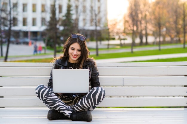 Portret van een gelukkige vrouwelijke studentenzitting op de bank met laptop in openlucht