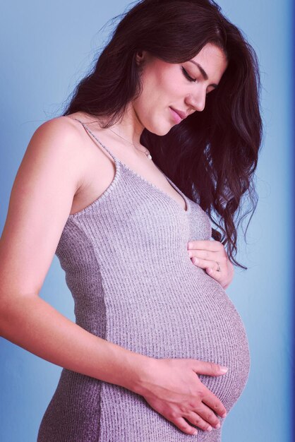 Portret van een gelukkige zwangere vrouw met handen op de buik geïsoleerd op een blauwe achtergrond