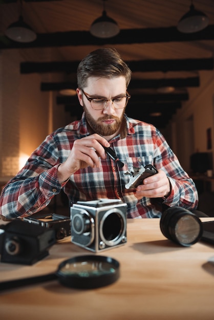 Portret van een gerichte jonge man die retro camera op zijn werkplek repareert