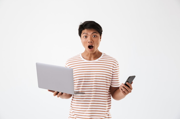 Portret van een geschokte jonge Aziatische laptop van de mensenholding