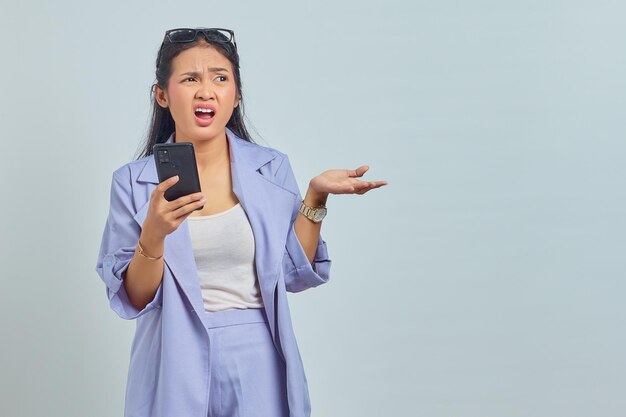 Portret van een geschokte jonge Aziatische vrouw die een mobiele telefoon vasthoudt en opzij kijkt met open mond geïsoleerd op een witte achtergrond