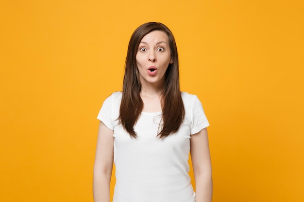 Portret van een geschokte jonge vrouw in witte vrijetijdskleding die de mond openhoudt, op zoek naar een camera geïsoleerd op een felgele oranje muurachtergrond in de studio. Mensen levensstijl concept. Bespotten kopie ruimte.