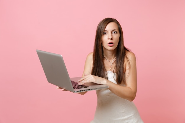 Portret van een geschokte vrouw in een witte jurk, die op een laptop pc werkt