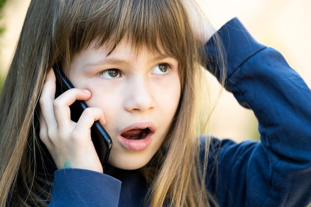 Portret van een gestrest kindmeisje met lang haar dat op een mobiele telefoon praat. Kleine vrouwelijke jongen communiceren met behulp van smartphone. Kinderen communicatieconcept.