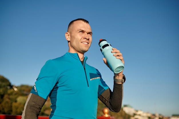Portret van een gezonde atletische man van middelbare leeftijd met een fit lichaam met een fles verfrissend water, rustend na het sporten of hardlopen. Mannelijke hardloper drinkt na buitentraining